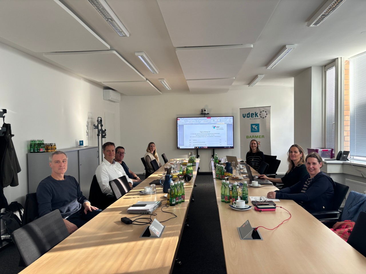 41. Sitzung des Steuerungsgremiums der regionalen BGF-Koordinierungsstelle Baden-Württemberg.Vier Frauen und drei Männer sitzend an zwei gegenüberstehenden Tischen mit einem Präsentationsbildschirm im Hintergrund. 