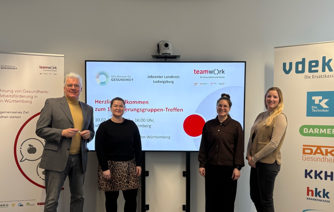 Vier Personen stehen vor einem Präsentationsbildschirm