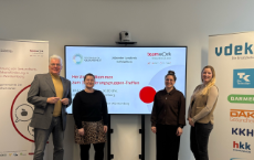 Vier Personen stehen vor einem Präsentationsbildschirm