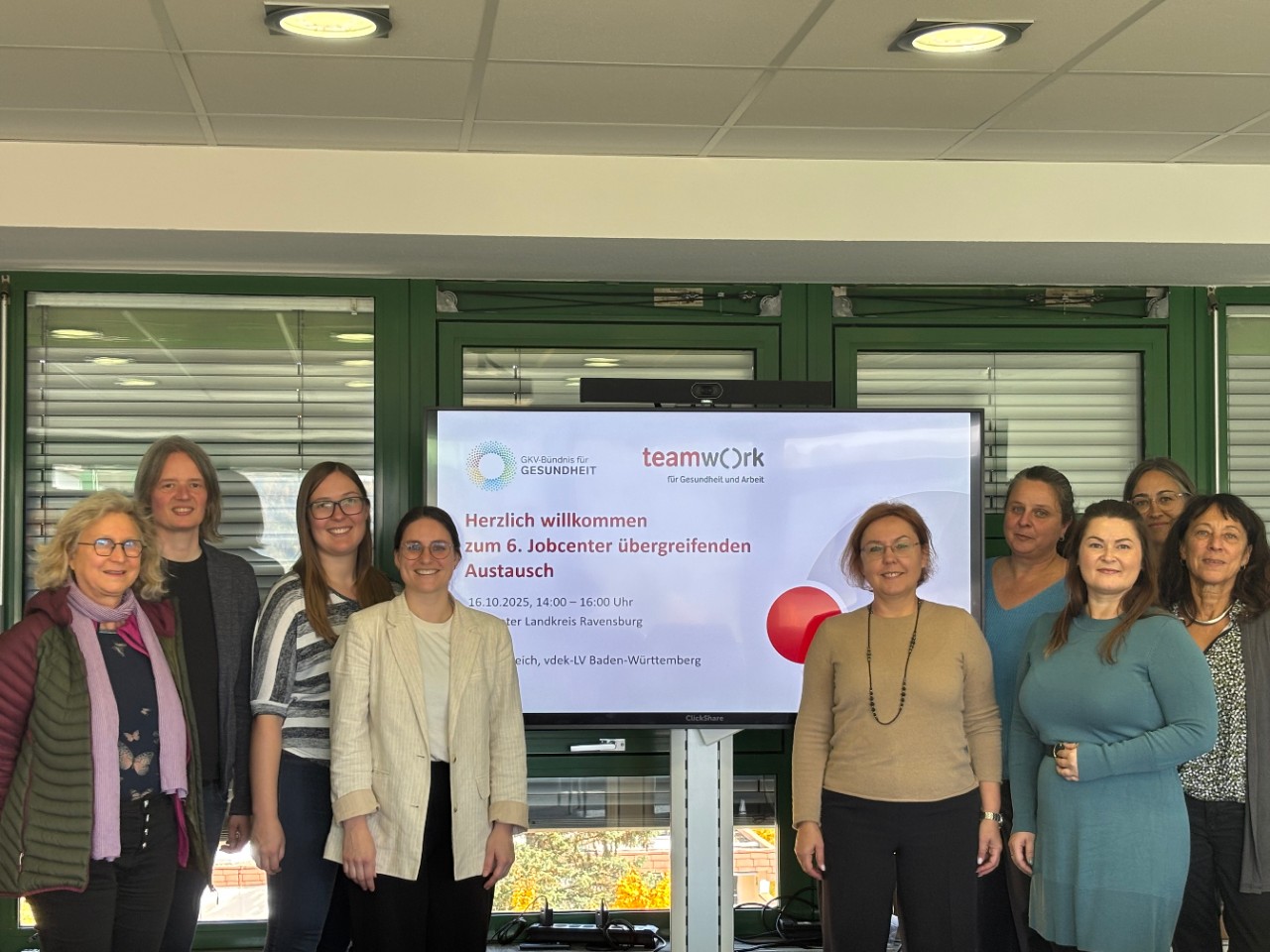 Neun Personen stehen vor einem Präsentationsbildschirm