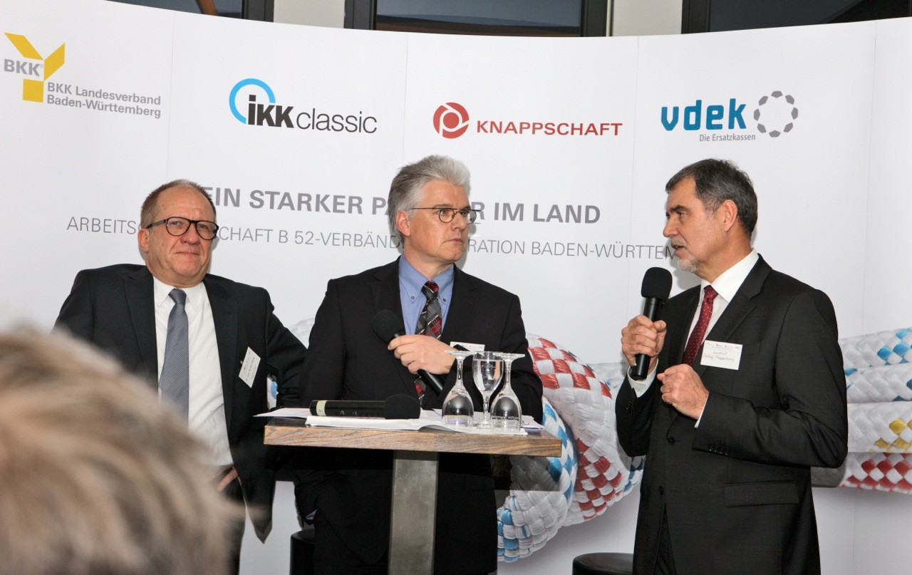 Dr. Norbert Metke, Frank Winkler und Landrat Detlef Piepenburg am Podium, Detlef Piepenburg hält ein Mikrofon und spricht