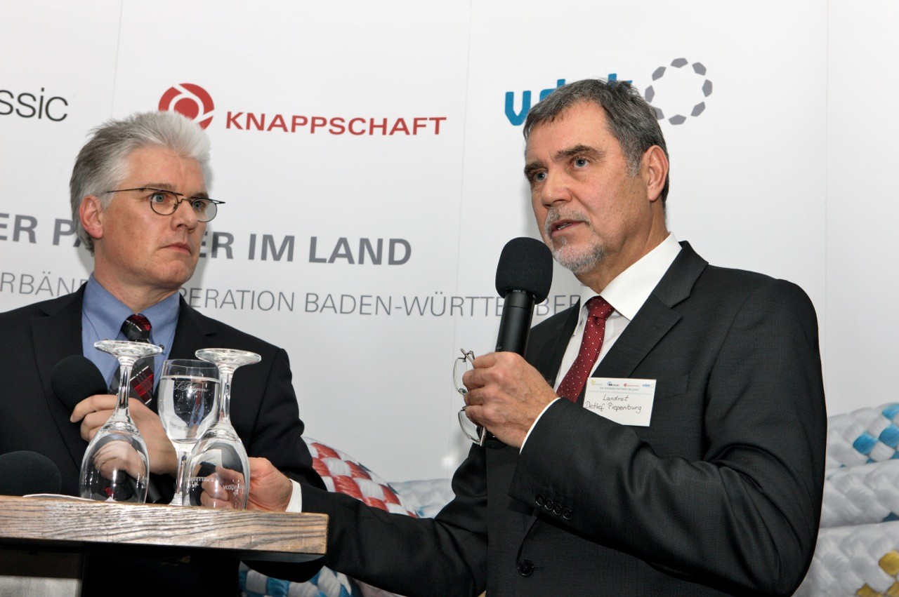 Frank Winkler und Landrat Detlef Piepenburg am Podium, Detlef Piepenburg hält ein Mikrofon und spricht