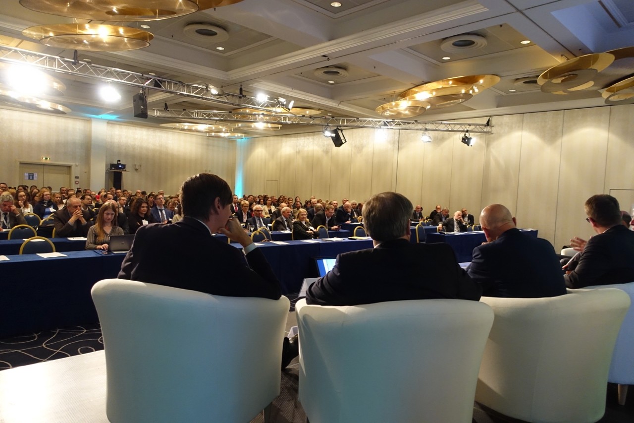 Vier Männer auf dem Podium blicken in den Saal