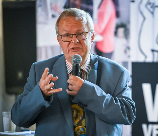 Ein Mann mit blauem Anzug , Brille und Mikrophon schaut in die Kamera