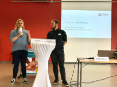 Frau mit Mikro und Mann am Stehpult