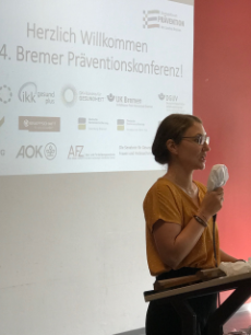 Frau Mit Brille und Mikro vor Präsentation