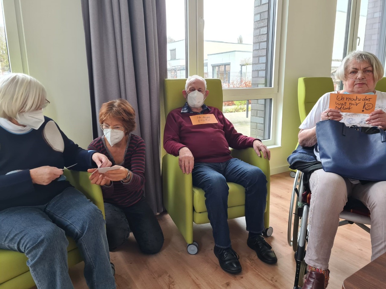 Drei alte Leute auf Stühlen und eine Therapeutin halten Zettel