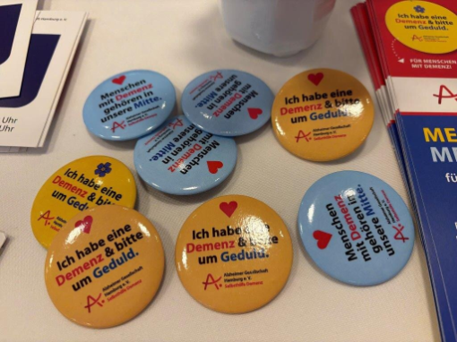 Tisch mit bunten Ansteckern mit der Aufschrift "Ich habe eine Demenz und bitte um Geduld"