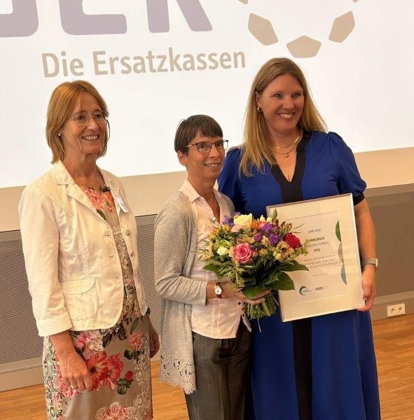 Drei Frauen mit Blumenstrauß und Urkunde bei Verleihung des Hamburger Selbsthilfepreises