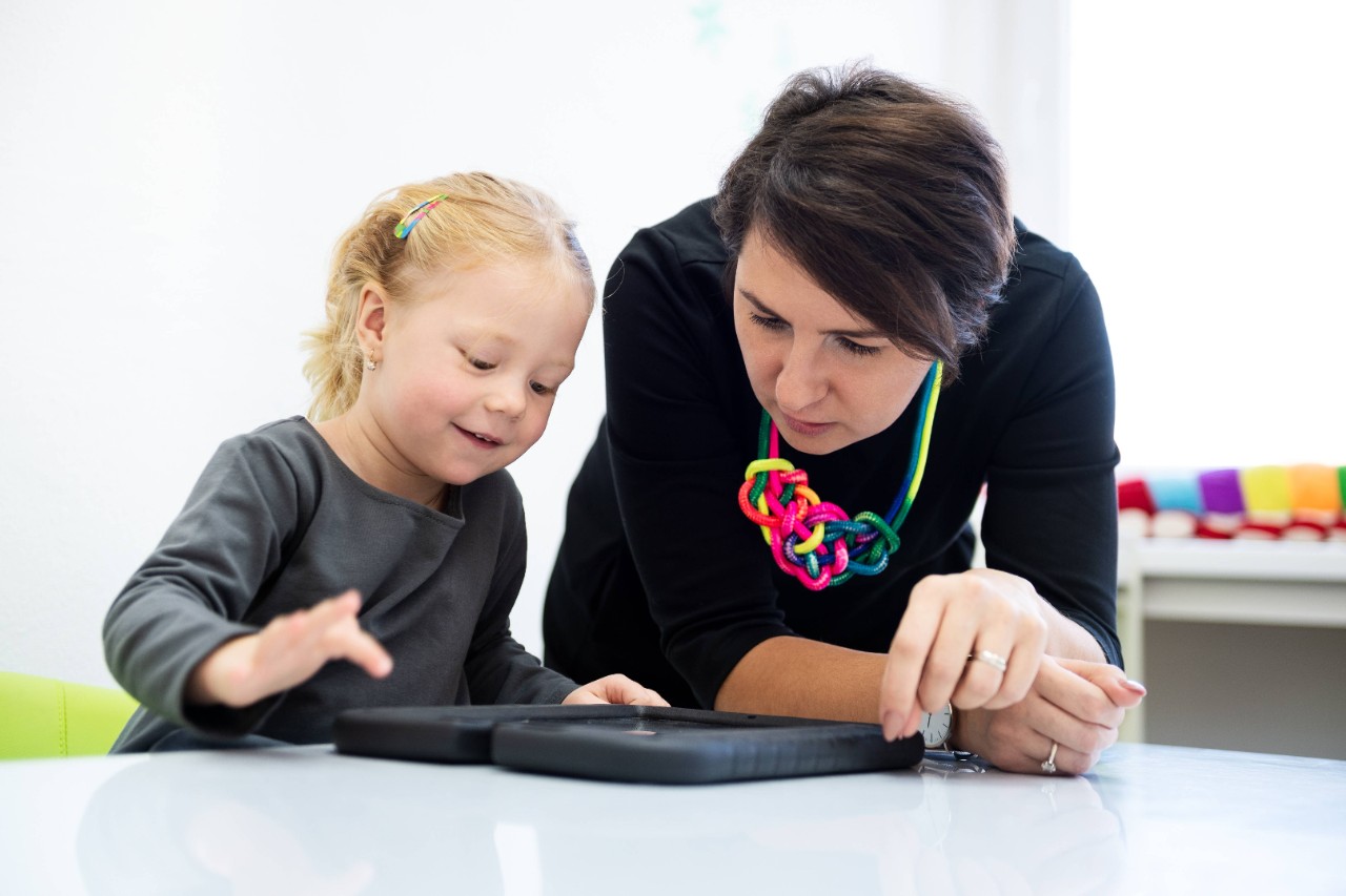 Ein kleines Mädchen macht mit ihrer Therapeutin spielerische Übungen auf einem Tablet-Computer