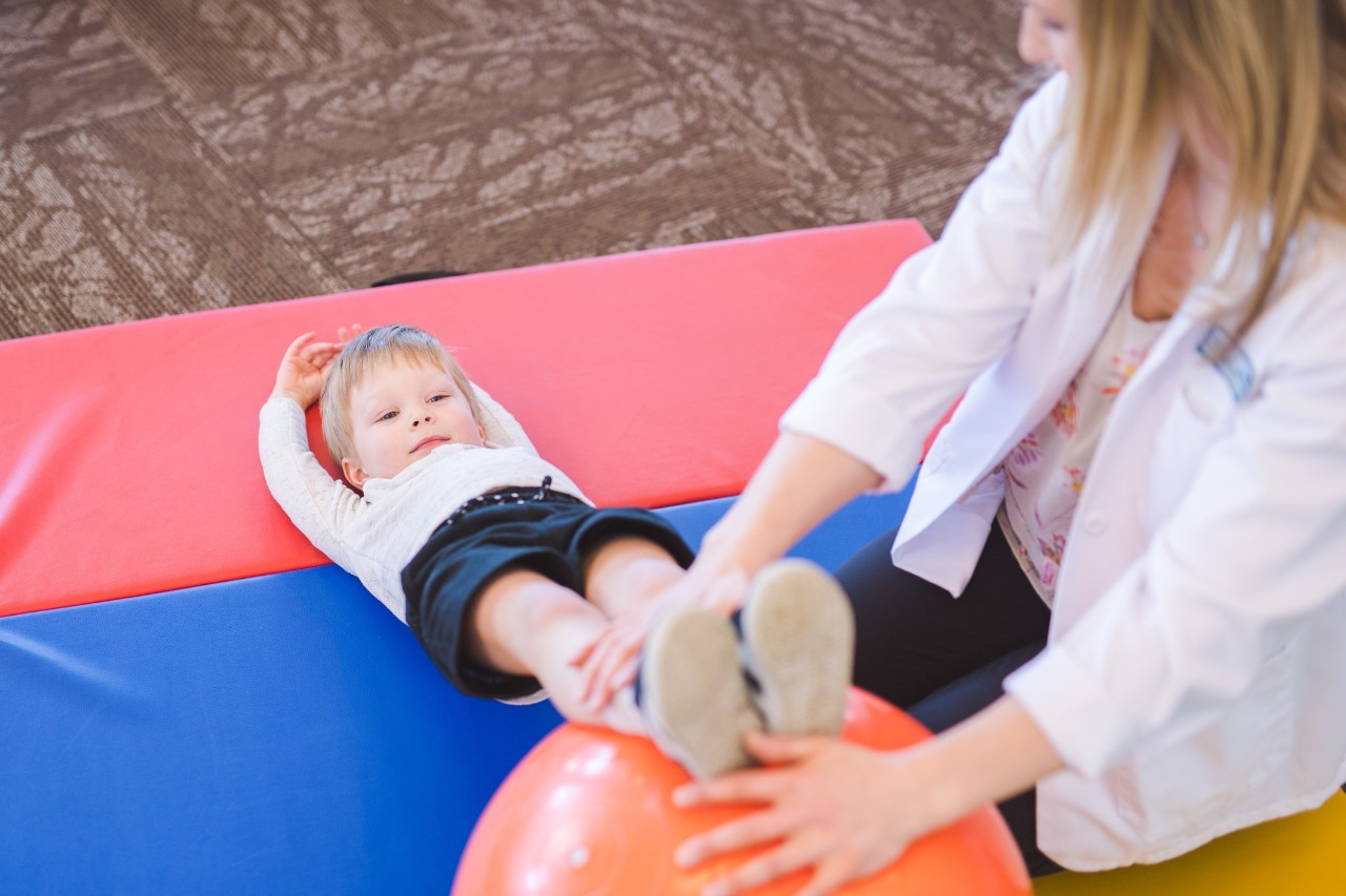 Eine Physiotherapeutin macht mit einem kleinen Jungen Übungen auf einer Bodenmatte