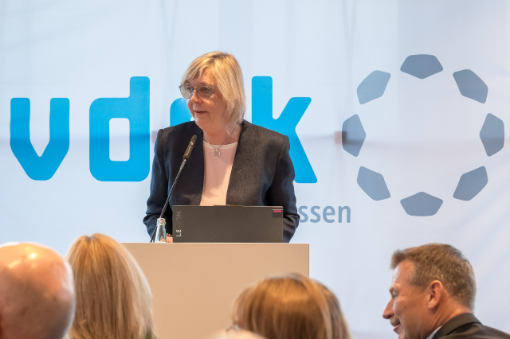 Frau am Rednerpult vor Banner mit Logo