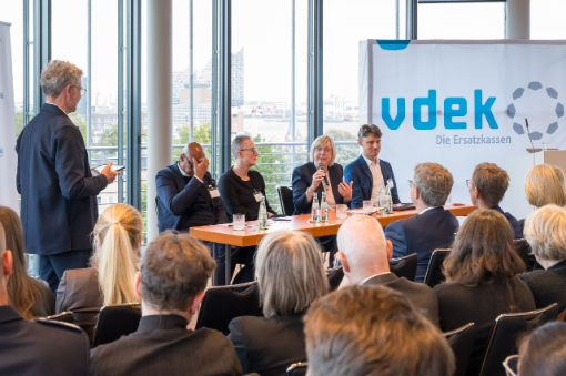 Podiumsdiskussion mit Moderator und zwei Frauen sowie zwei Männern vor Publikum