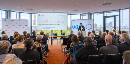 Gäste in vollbesetztem Saal mit Mann am Rednerpult