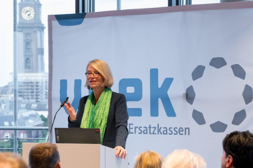 Frau hält Rede an Rednerpult vor Banner mit Logo