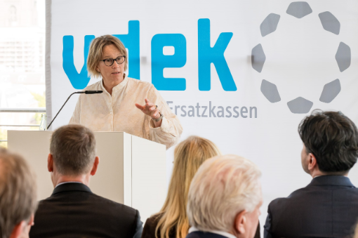 Frau an Rednerpult vor Banner mit Logo