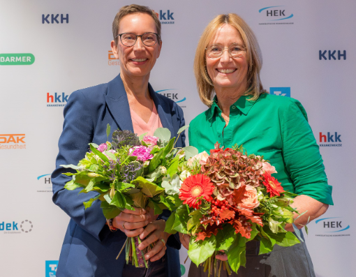 Zwei Frauen mit Blumensträußen vor Banner mit Logos
