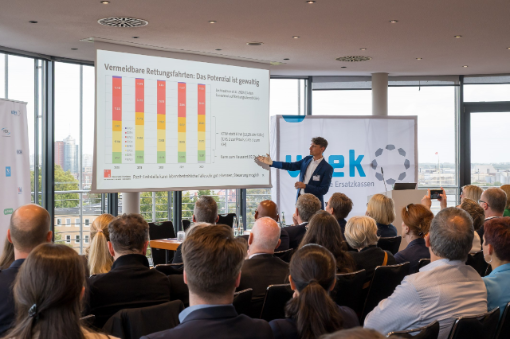 Mann erklärt Powerpoint-Folie vor Gästen in vollbesetztem Saal