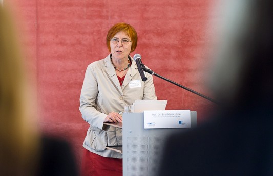 Blick zwischen den K&ouml;pfen des Publikums hindurch auf Prof. Dr. Eva-Maria Ulmer, welche am Rednerpult steht und spricht