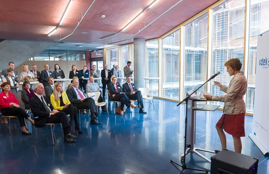 Prof. Dr. Eva-Maria Ulmer, rechts im Bild, steht am Rednerpult und spricht zum Publikum, welches links im Bild sitzt