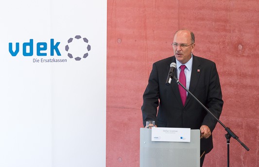 Sozialminister Stefan Gr&uuml;ttner steht am Rednerpult und spricht, links von ihm steht ein vdek-Banner