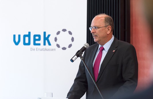 Sozialminister Stefan Gr&uuml;ttner steht am Rednerpult und spricht, links von ihm steht ein vdek-Banner