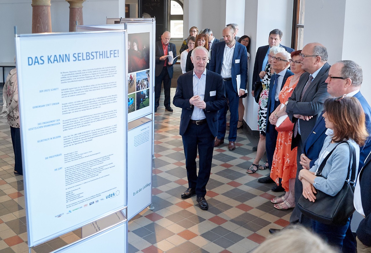 Manfred Wigger, Kurator der vdek-Fotoausstellung, erl&auml;utert den G&auml;sten die Fotografien