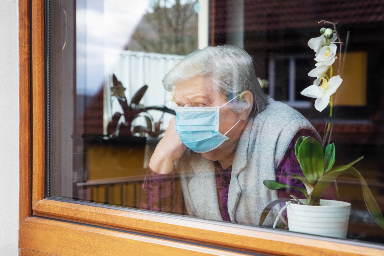 Seniorin mit Maske am Fenster