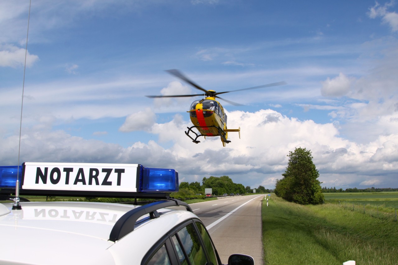 Notarztfahrzeug am Straßenrand un Rettungshubschrauber im Landeanflug