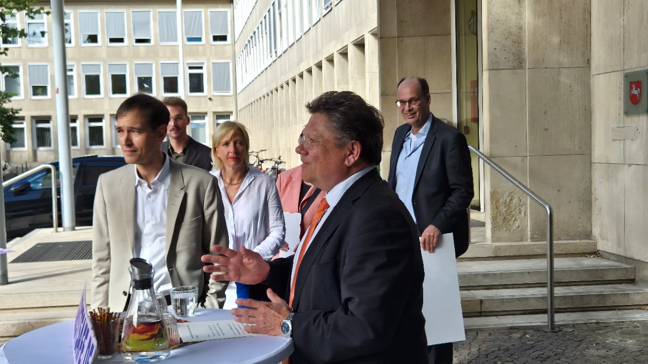 Ein Mann spricht an einem runden Tisch, andere h&ouml;ren zu