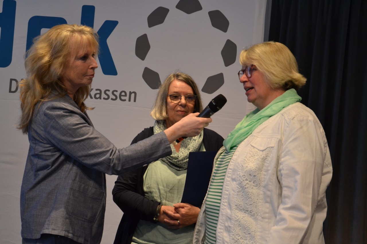 Eine Frau mit einem Mikrofon in der Hand interviewt eine andere Frau. Eine weitere Frau steht im Hintergrund.