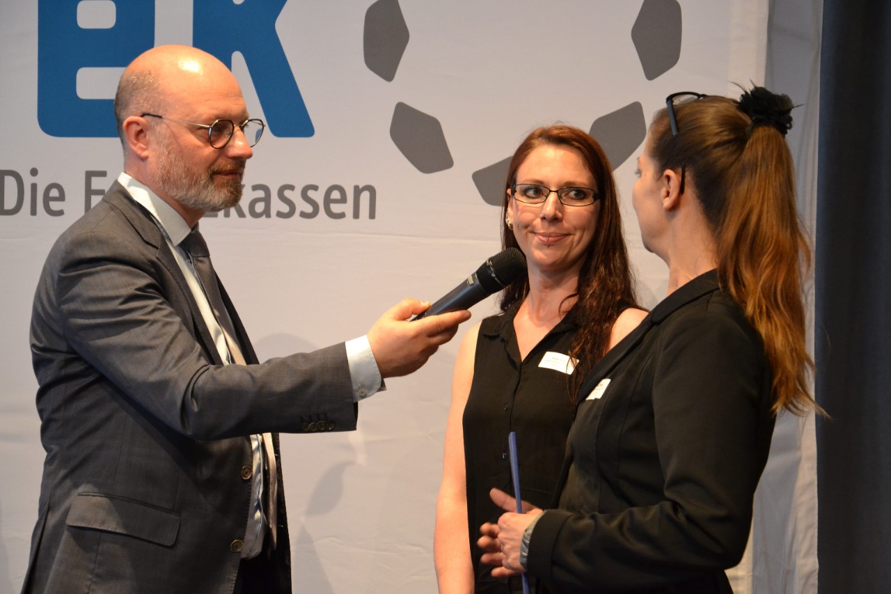 Ein Mann mit einem Mikrofon in der Hand interviewt zwei Frauen