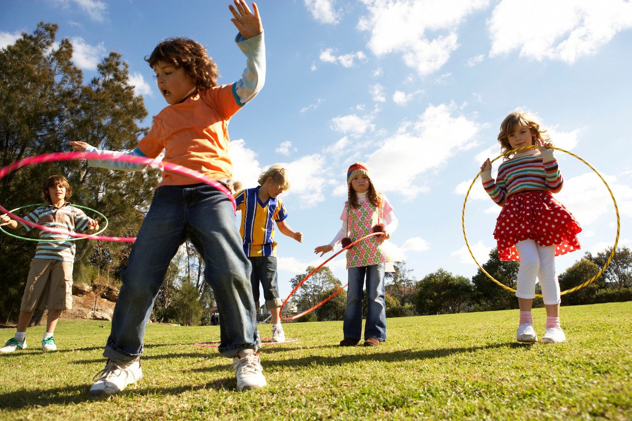 Kinder auf einer Wiese mit Hula Hoop Reifen