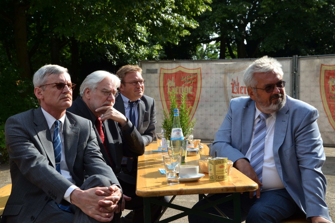 Dr. Kriedel, Dr. Potthof, Dr. Schmitz und Dr. Dryden sitzen an einem Tisch