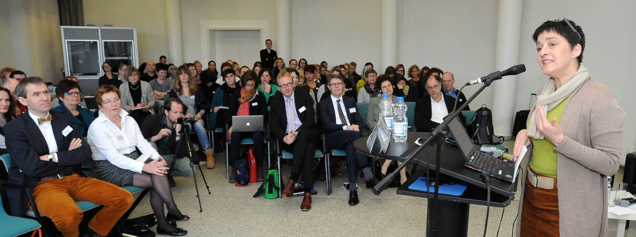 NRW Gesundheitsministerin Barbara Steffens am Rednerpult und große Zuschauerrunde