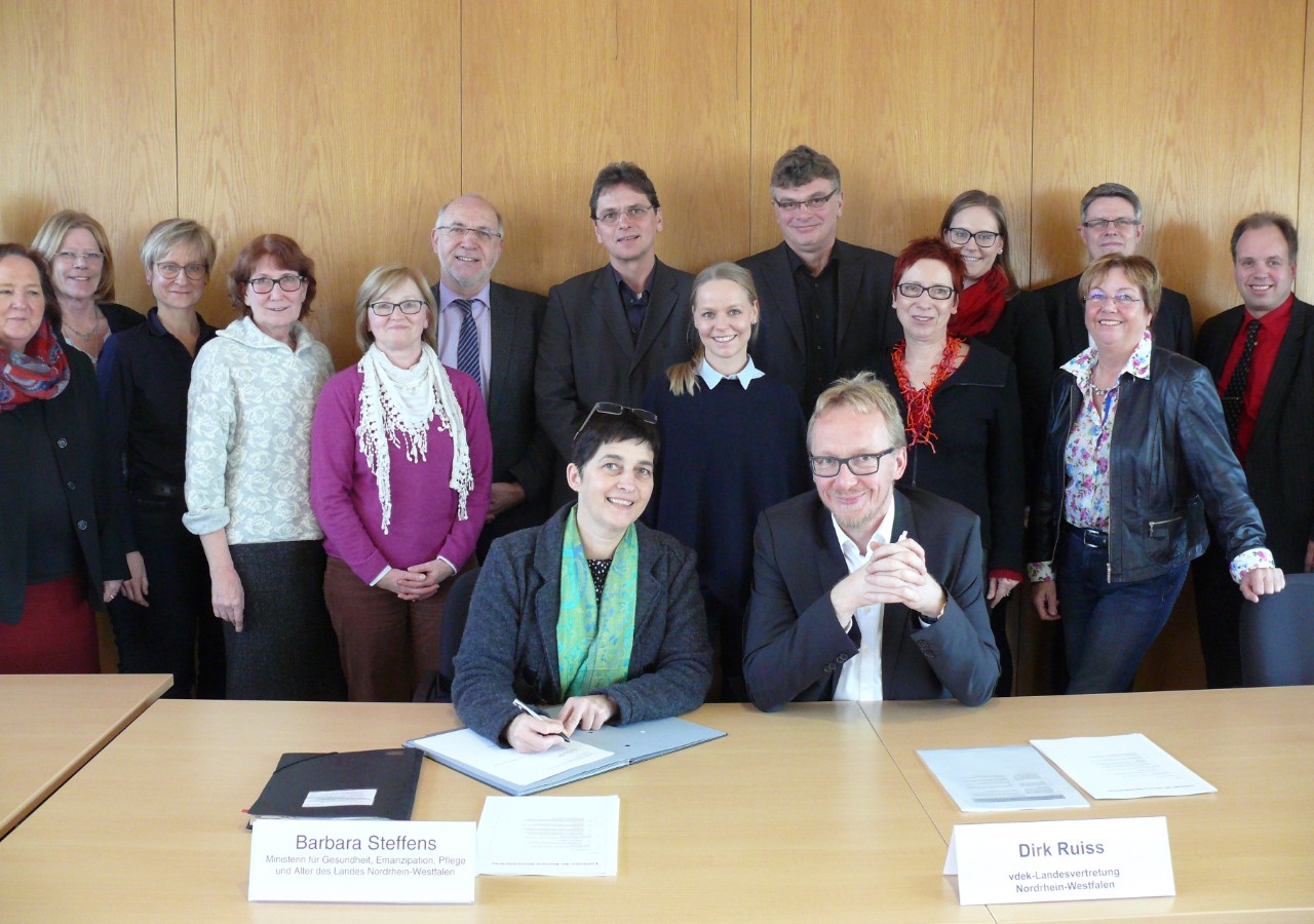 Herr Ruiss vom vdek und NRW Gesundheitsministerin Barbara Steffens unterzeichnen einen Vertrag - im Hintergrund 14 weitere Personen
