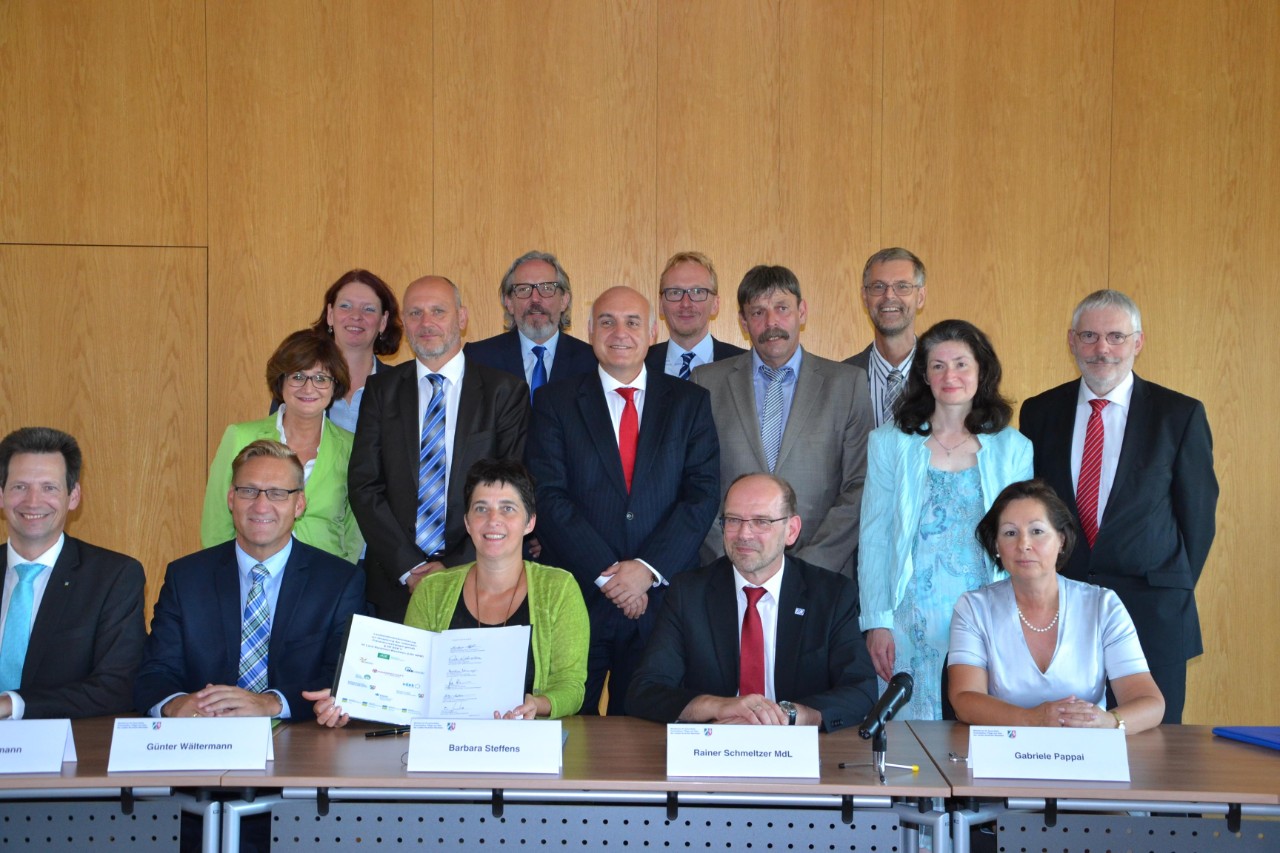 NRW Gesundheitsministerin Barbara Steffens und vier weitere Menschen sitzen an einem Tisch und pr&auml;sentieren den unterschriebenen Vertrag
