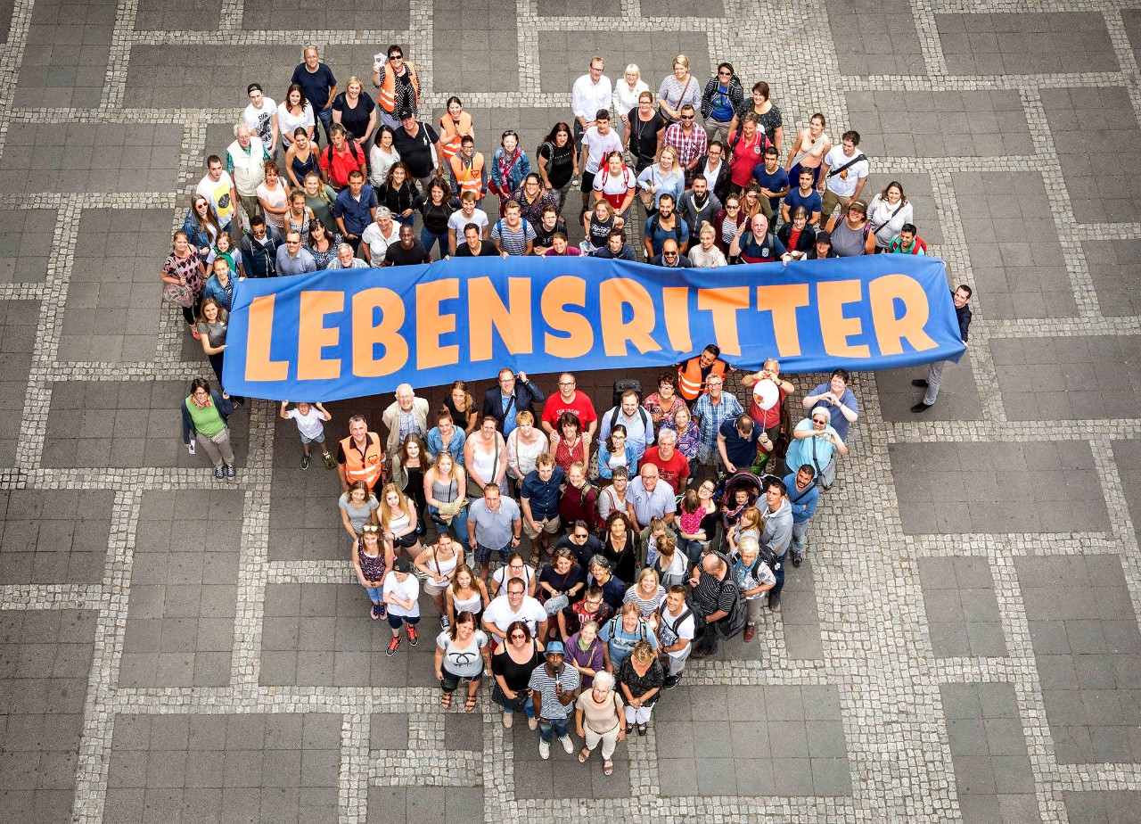 Blick aus großer Höhe auf eine Menschengruppe in Herzform mit dem Schild Lebensritter
