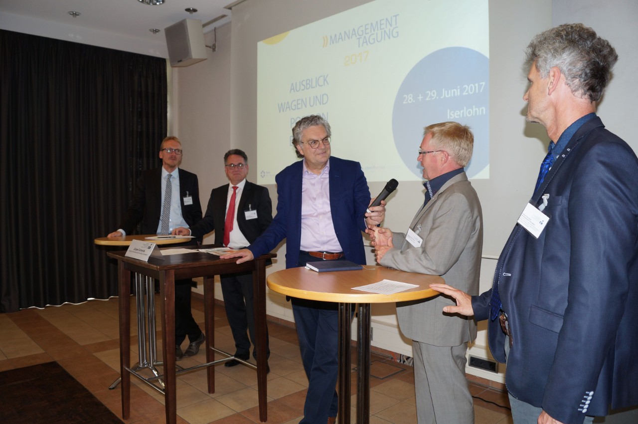 Fünf Männer an Stehpulten diskutieren
