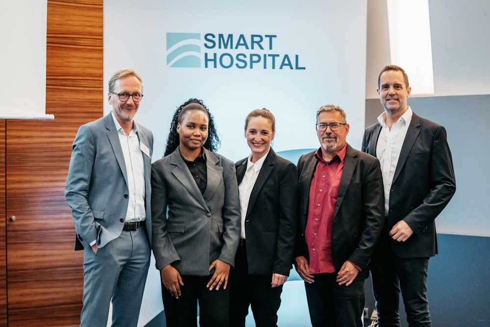 Fünf Personen stehen nebeneinander unterhalb eines Plakats mit der Aufschrift "Smart Hospital"