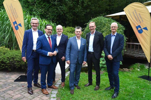 Sechs Männer im Anzug draußen zwischen Beachflags