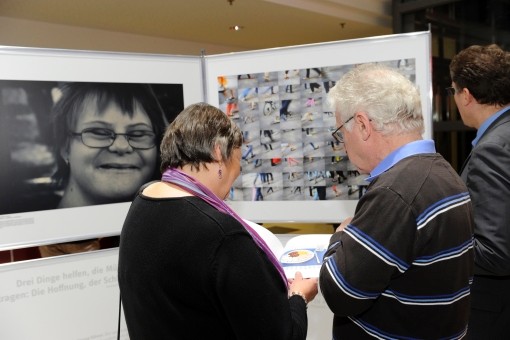 G&auml;ste der Ausstellung stehen vor ausgestellten Fotografien und schauen in den dazugeh&ouml;rigen Katalog