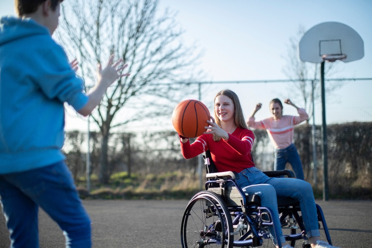 Mädchen im Rollstuhl spielt Basketball mit Freunden