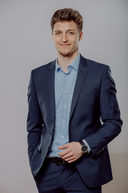 Ein Mann im dunkelblauen Anzug steht vor einer grauen Wand