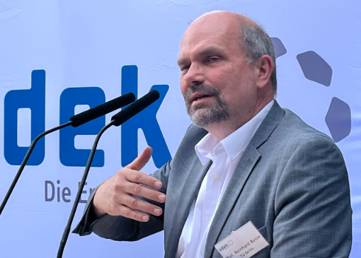 Ein Mann mit Halbglatze und Bart spricht in ein Mikrofon und gestikuliert - im Hintergrund das Logo des vdek Ein Mann mit Halbglatze und Bart spricht in ein Mikrofon und gestikuliert - im Hintergrund das Logo des vdek
