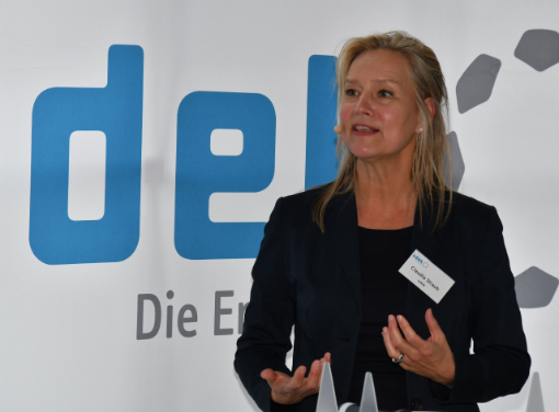 Eine blonde Frau in einem dunkelblauen Blazer steht vor dem Logo des vdek und redet mit aktiver Körpersprache