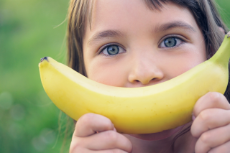 Face of a beautiful young Caucasian girl with banana smile on nature background.