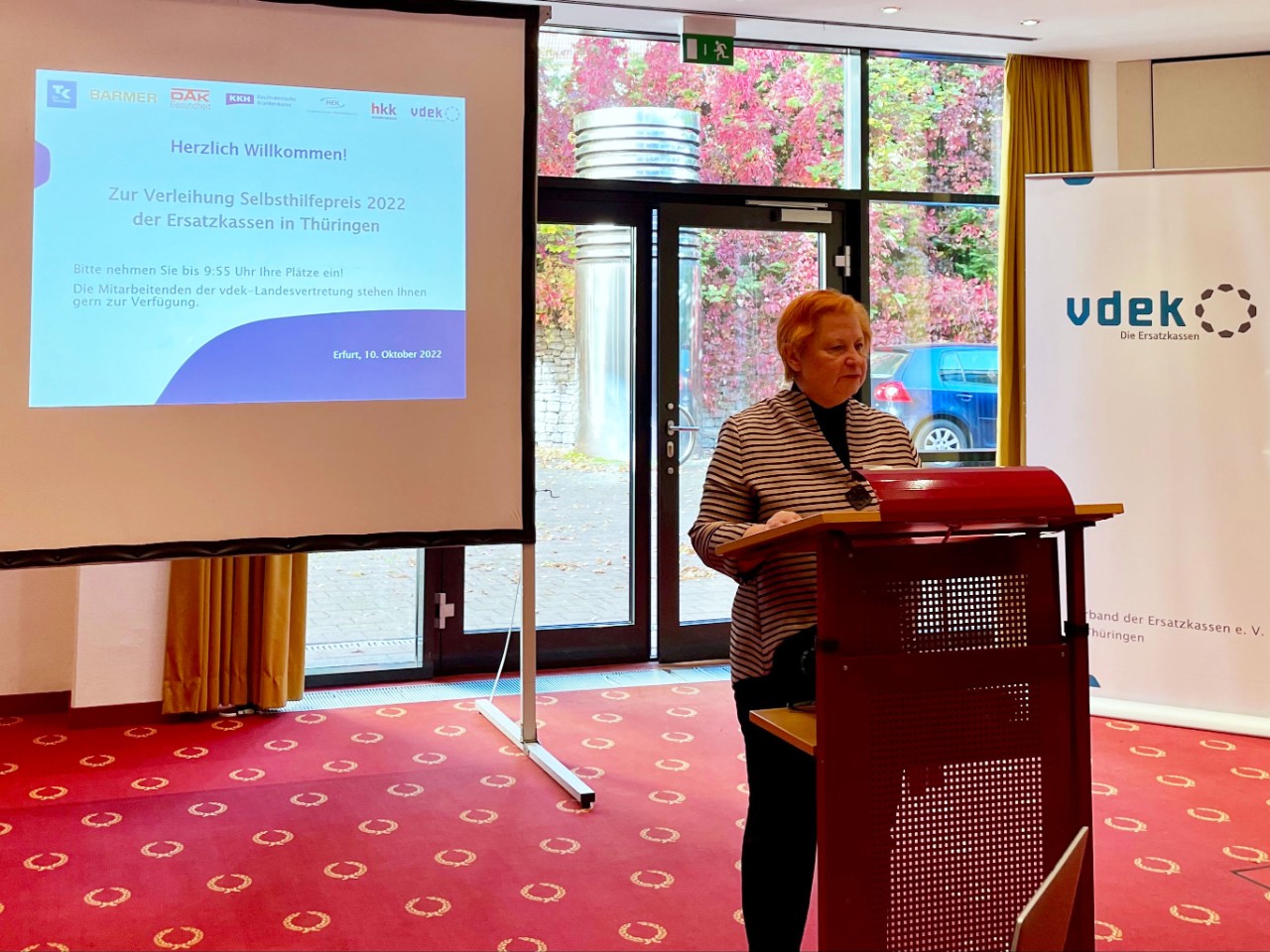 Frau an Rednerpult vor einer PowerPoint Präsentation