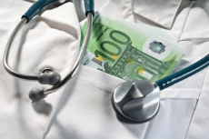 100-Euro-Scheine stecken in der Brusttasche eines Arztkittels, auf dem ein Stetoskop liegt