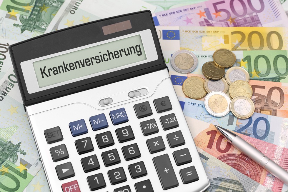 Das Wort "Krankenkasse" steht auf dem Display eines Taschenrechners, der auf Euroscheinen und Münzen liegt Das Wort "Krankenkasse" steht auf dem Display eines Taschenrechners, der auf Euroscheinen und Münzen liegt